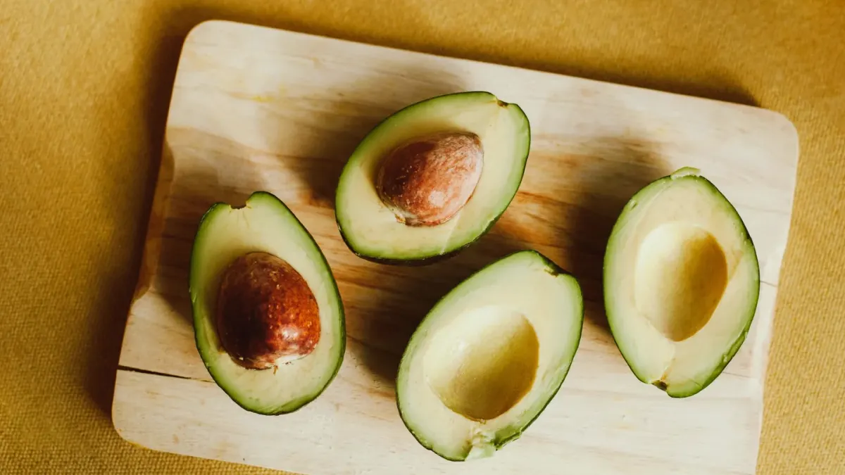 A halved avocado on a cutting board while a dog watches from the kitchen floor