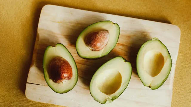 A halved avocado on a cutting board while a dog watches from the kitchen floor