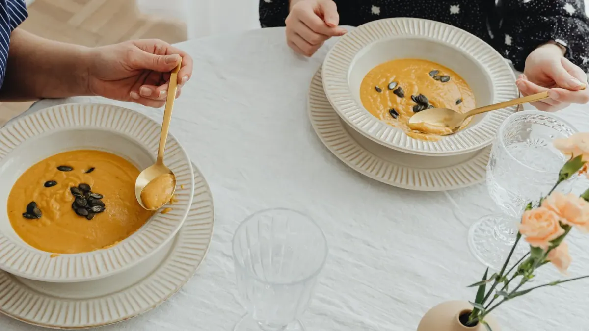 A spoon lifting orange pumpkin puree over a stainless dog bowl
