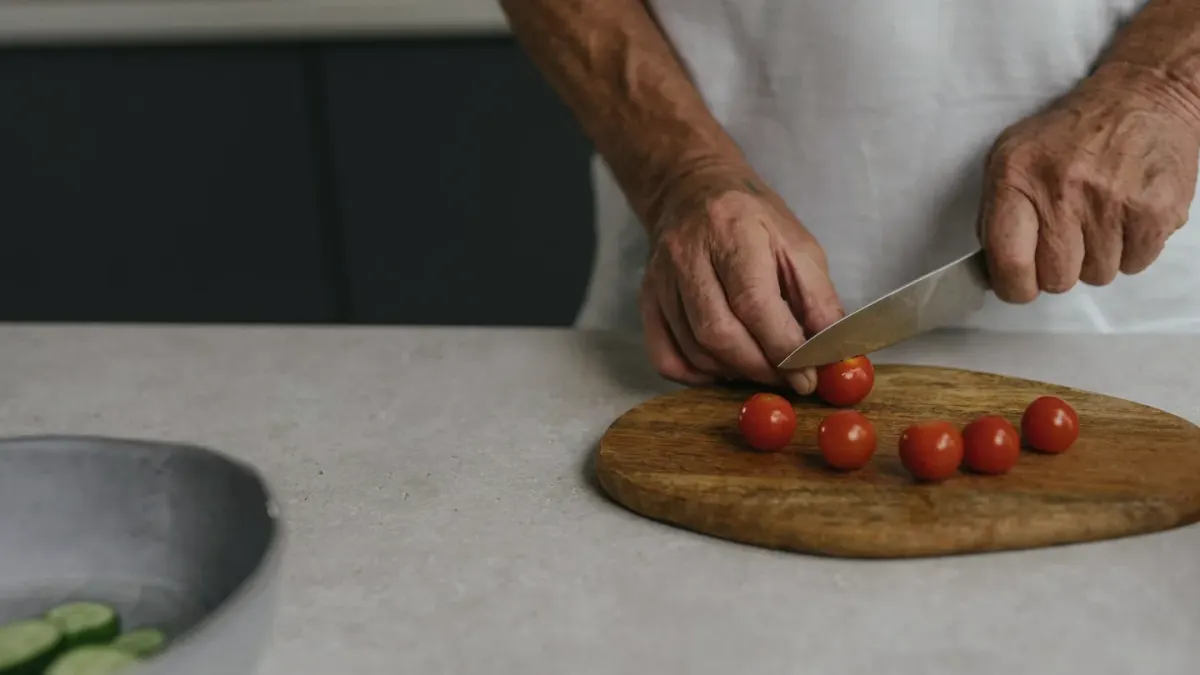 Hands slicing a red apple on a cutting board while a dog waits nearby